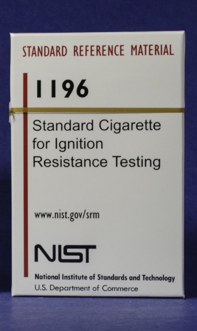 A pack of cigarettes labeled "Standard Reference Material" and "Standard Cigarette for Ignition Resistance Testing" in red and black text on a plain white box with the NIST logo.